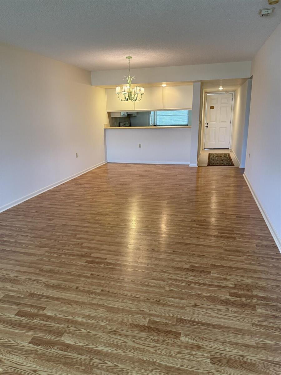 An open living area features light wood-look flooring, a chandelier, and a kitchen pass-through window — 3710 Whitehall Drive # 401, West Palm Beach FL 33401, WEST PALM BEACH, FL