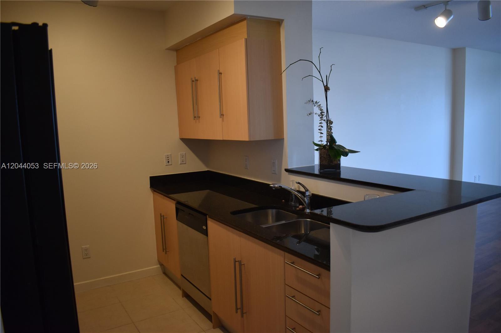 A kitchen features light wood cabinets, black countertops, stainless steel appliances, and a breakfast bar — 325 S Biscayne Blvd # 3616, Miami FL 33131, MIAMI, FL