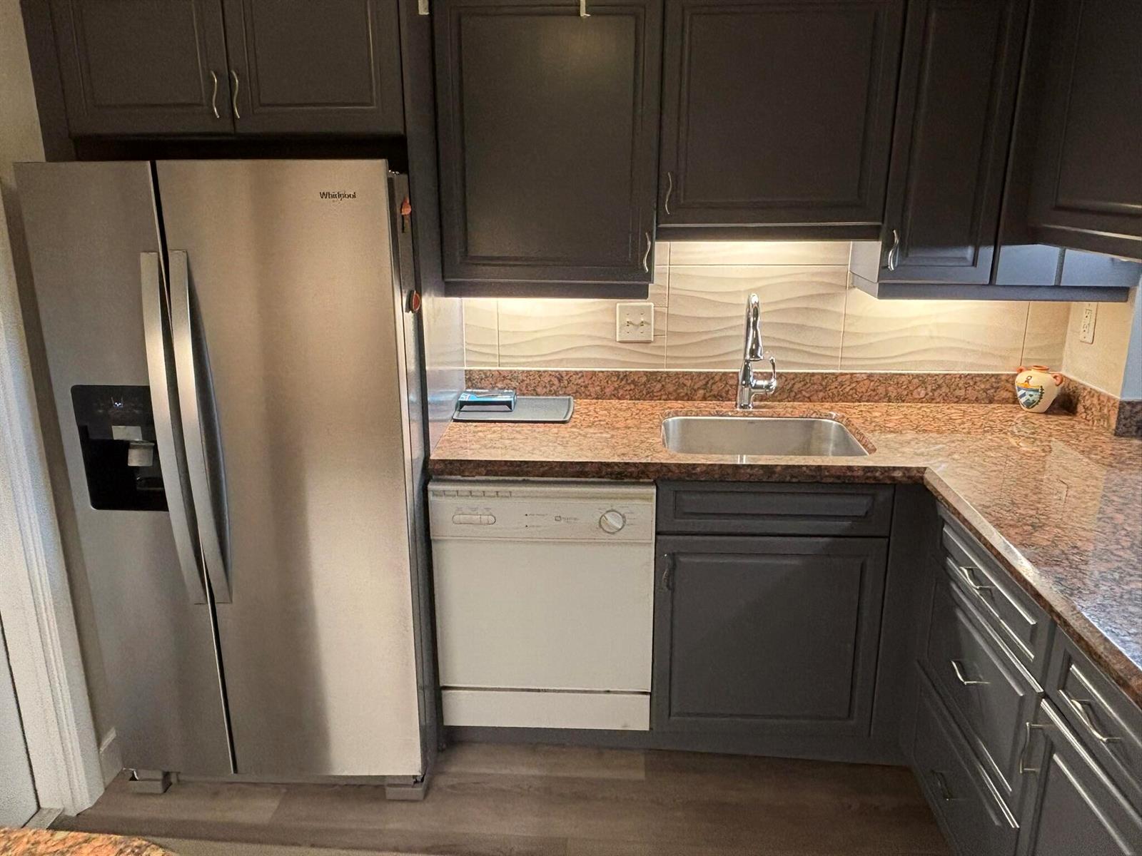 A kitchen features dark cabinets, granite countertops, a stainless steel refrigerator, and a white dishwasher — 2668 Garden Drive N # 312, FL 33461, FL