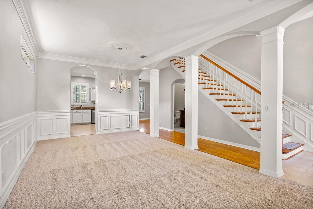A carpeted dining area features a chandelier, wainscoting, and an adjacent staircase with wooden treads — 5612 ROCKFIELD LOOP, VALRICO, FL