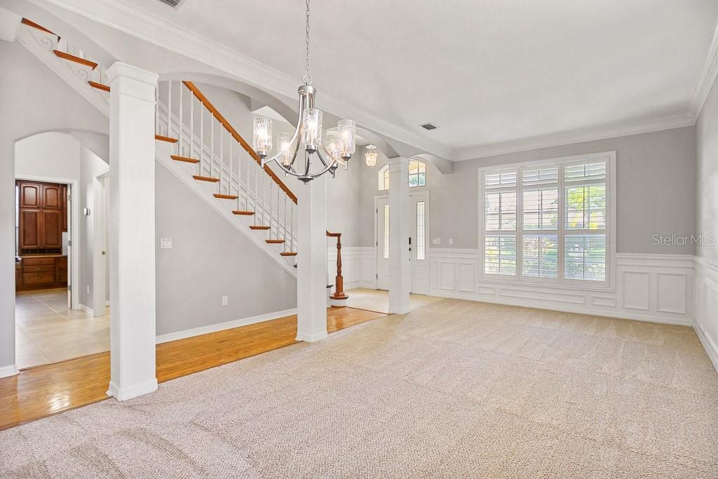 A carpeted living room features a staircase with wood railings and a central chandelier — 5612 ROCKFIELD LOOP, VALRICO, FL