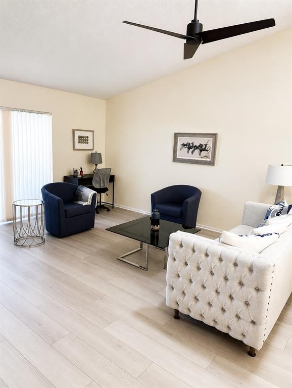 A living room features a tufted sofa, two navy armchairs, a glass coffee table, and wood-look flooring — 1211 CAPRI ISLES BOULEVARD UNIT 122, VENICE, FL