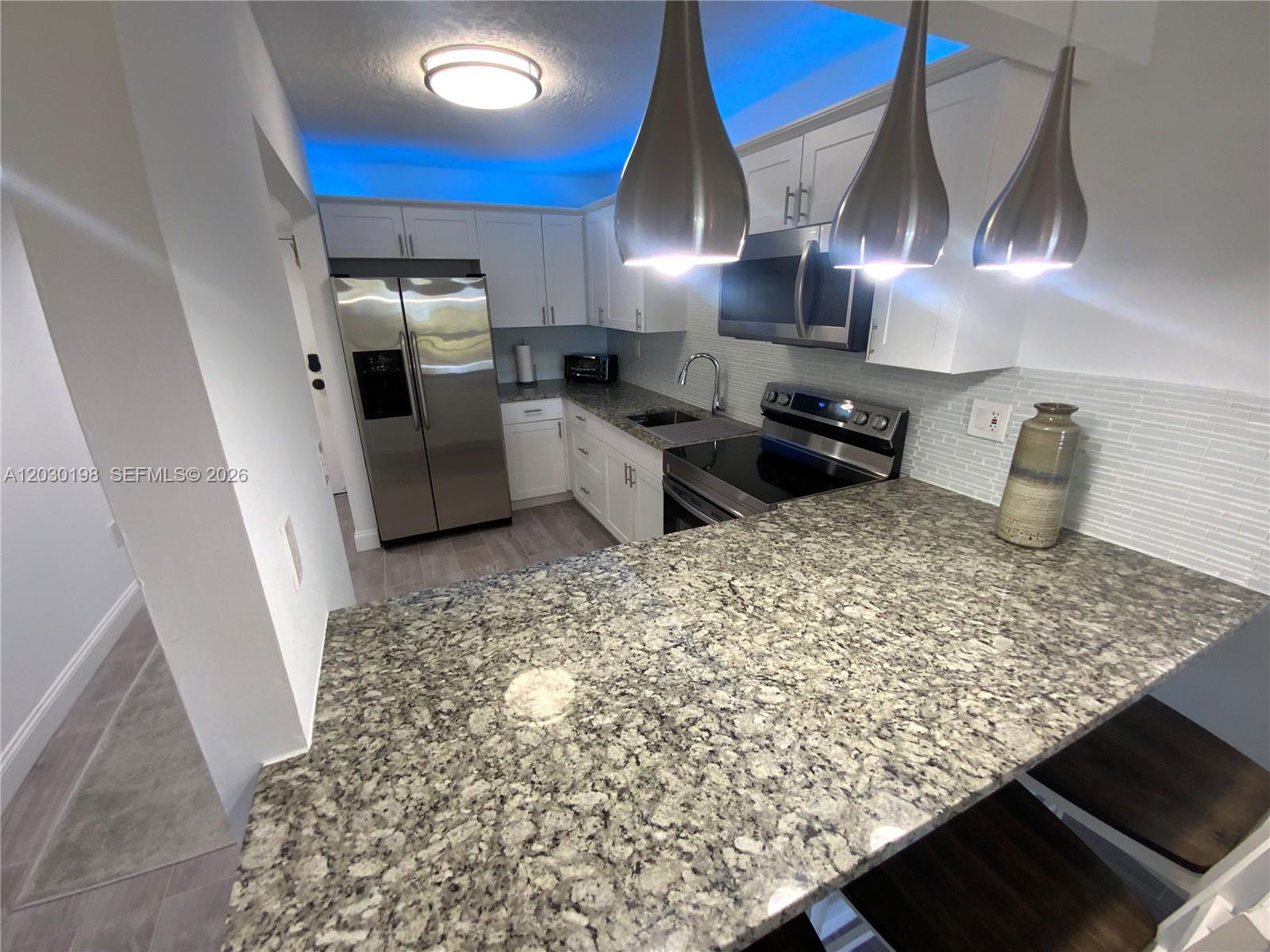 A kitchen features white cabinets, granite countertops, stainless steel appliances, and blue accent lighting — 6444 Collins Ave # A6, Miami Beach FL 33141, MIAMI BEACH, FL