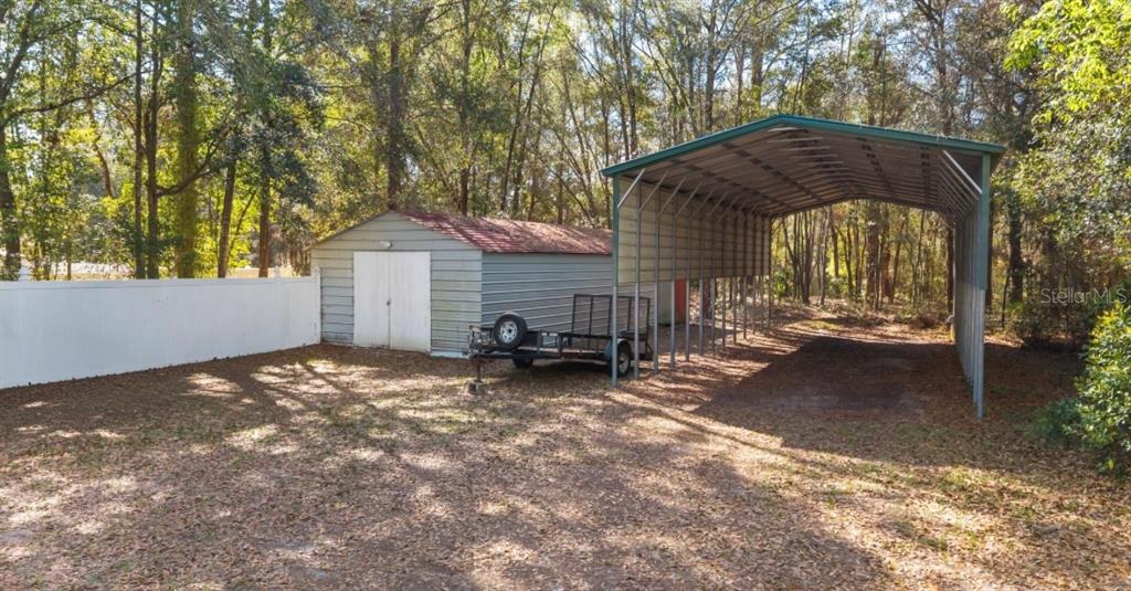 A metal shed and an attached open-sided carport stand in a wooded backyard — 8599 N MESSINA LOOP, CRYSTAL RIVER, FL
