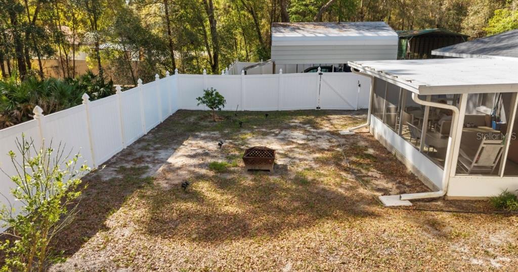 A fenced backyard features a fire pit, a small tree, and a screened-in patio — 8599 N MESSINA LOOP, CRYSTAL RIVER, FL