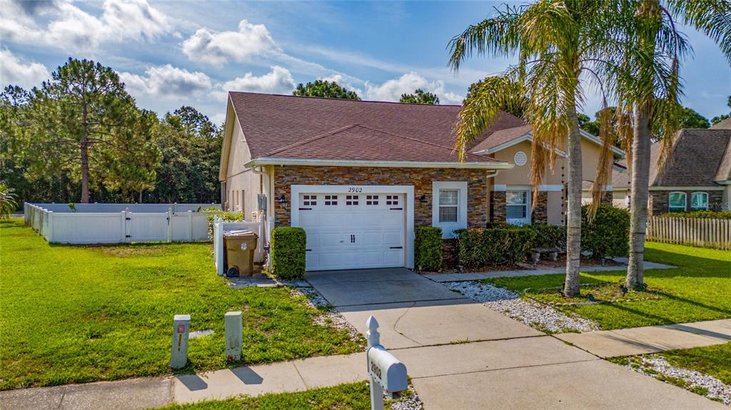 A single-story house with a stone-accented garage, a white fence, and palm trees — 2902 PADDINGTON WAY, KISSIMMEE, FL