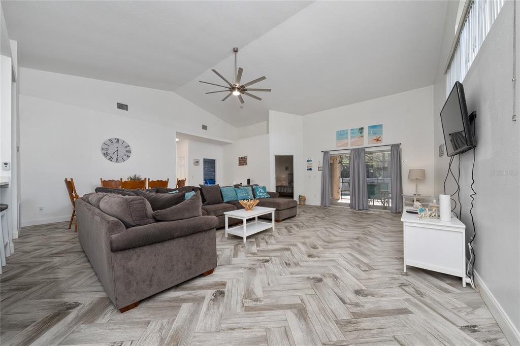 A living room features a large gray sectional sofa, herringbone wood-look flooring, and vaulted ceilings — 2902 PADDINGTON WAY, KISSIMMEE, FL