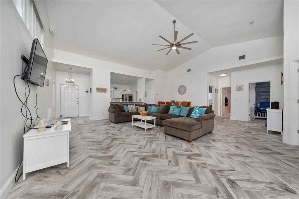 A spacious living room features a large brown sectional, vaulted ceilings, and herringbone-patterned wood flooring — 2902 PADDINGTON WAY, KISSIMMEE, FL