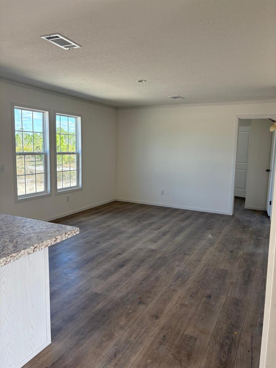 An empty room with wood-look flooring, white walls, and two windows overlooking a wooded area — 15983 NW 272nd Street, Okeechobee FL 34972, OKEECHOBEE, FL