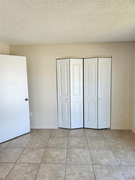 A room with beige walls, a popcorn ceiling, tiled flooring, and white closet doors — 1882 CARALEE BOULEVARD UNIT 3, ORLANDO, FL