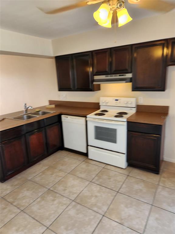 A kitchen features dark wood cabinets, tan countertops, a white stove, and tiled flooring — 1882 CARALEE BOULEVARD UNIT 3, ORLANDO, FL