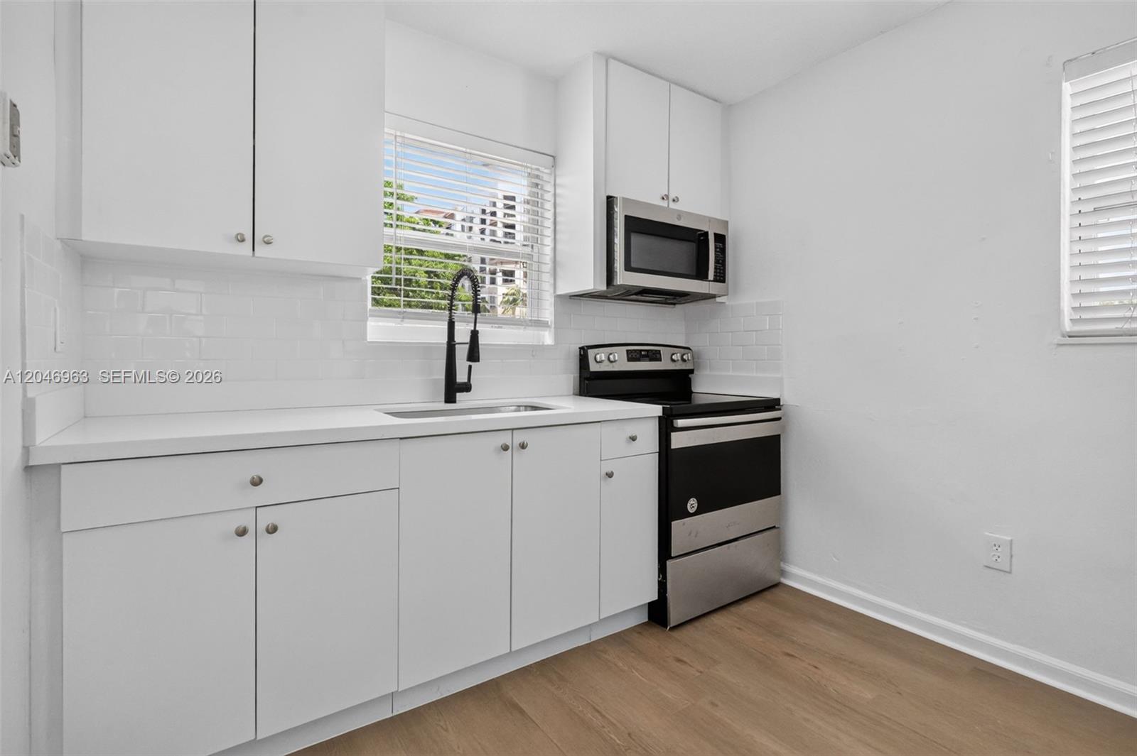 A small kitchen features white cabinets, stainless steel appliances, and light wood-look flooring — 458 SW 9th St # 1, Miami FL 33130, MIAMI, FL