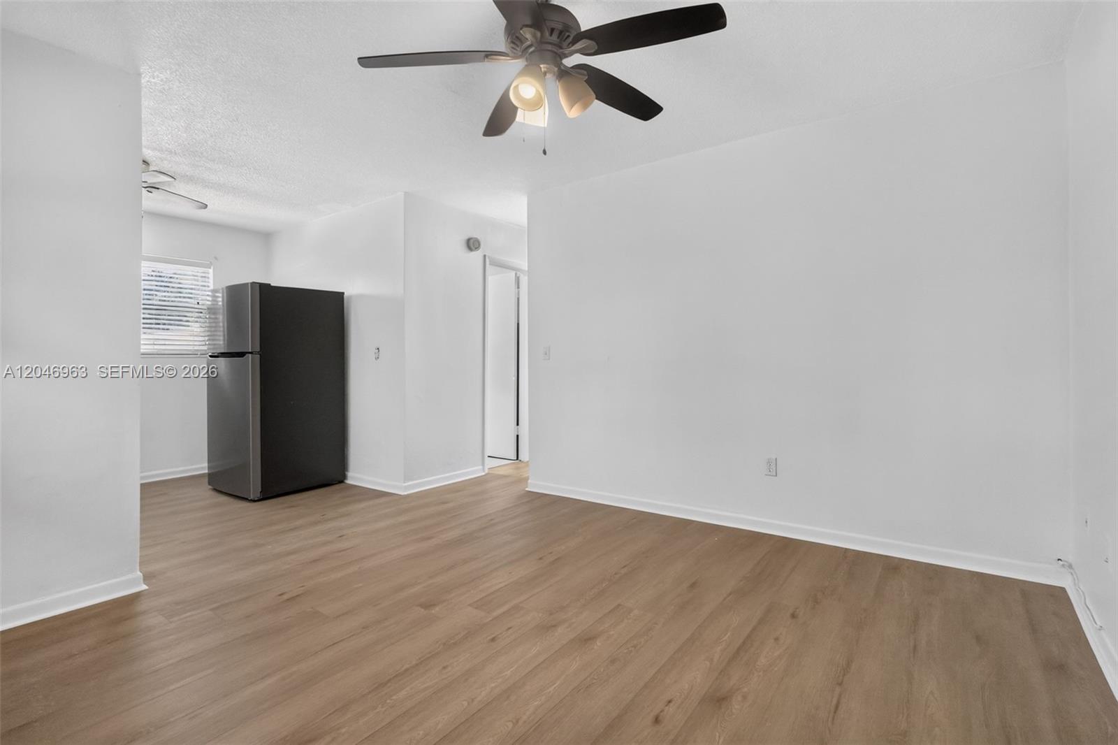 An empty room features light wood-look flooring, white walls, a ceiling fan, and a black refrigerator — 458 SW 9th St # 1, Miami FL 33130, MIAMI, FL