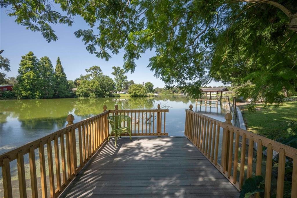 A wooden deck with railings overlooks a calm lake surrounded by trees — 1925 JOHN ARTHUR WAY, LAKELAND, FL