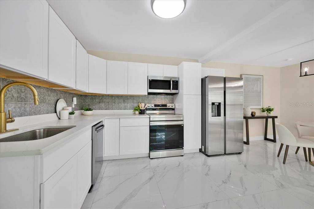A modern kitchen features white cabinets, stainless steel appliances, and marble-look tile flooring — 1925 JOHN ARTHUR WAY, LAKELAND, FL