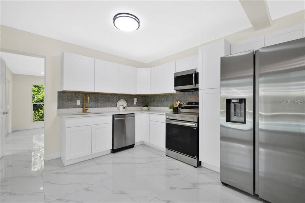 A kitchen features white cabinets, stainless steel appliances, a patterned backsplash, and marble-look tile flooring — 1925 JOHN ARTHUR WAY, LAKELAND, FL