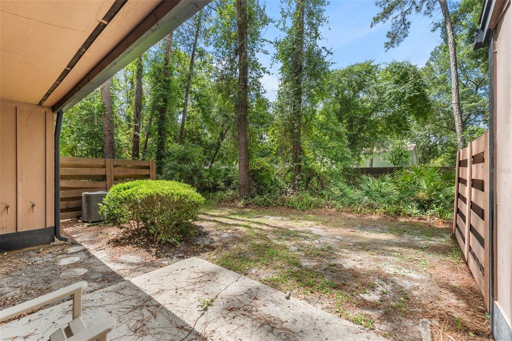 A concrete patio overlooks a small backyard with a bush and a wooden privacy fence — 2355 NW 45TH LANE, GAINESVILLE, FL