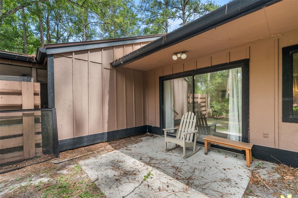 A concrete patio sits outside a sliding glass door with a wooden rocking chair — 2355 NW 45TH LANE, GAINESVILLE, FL