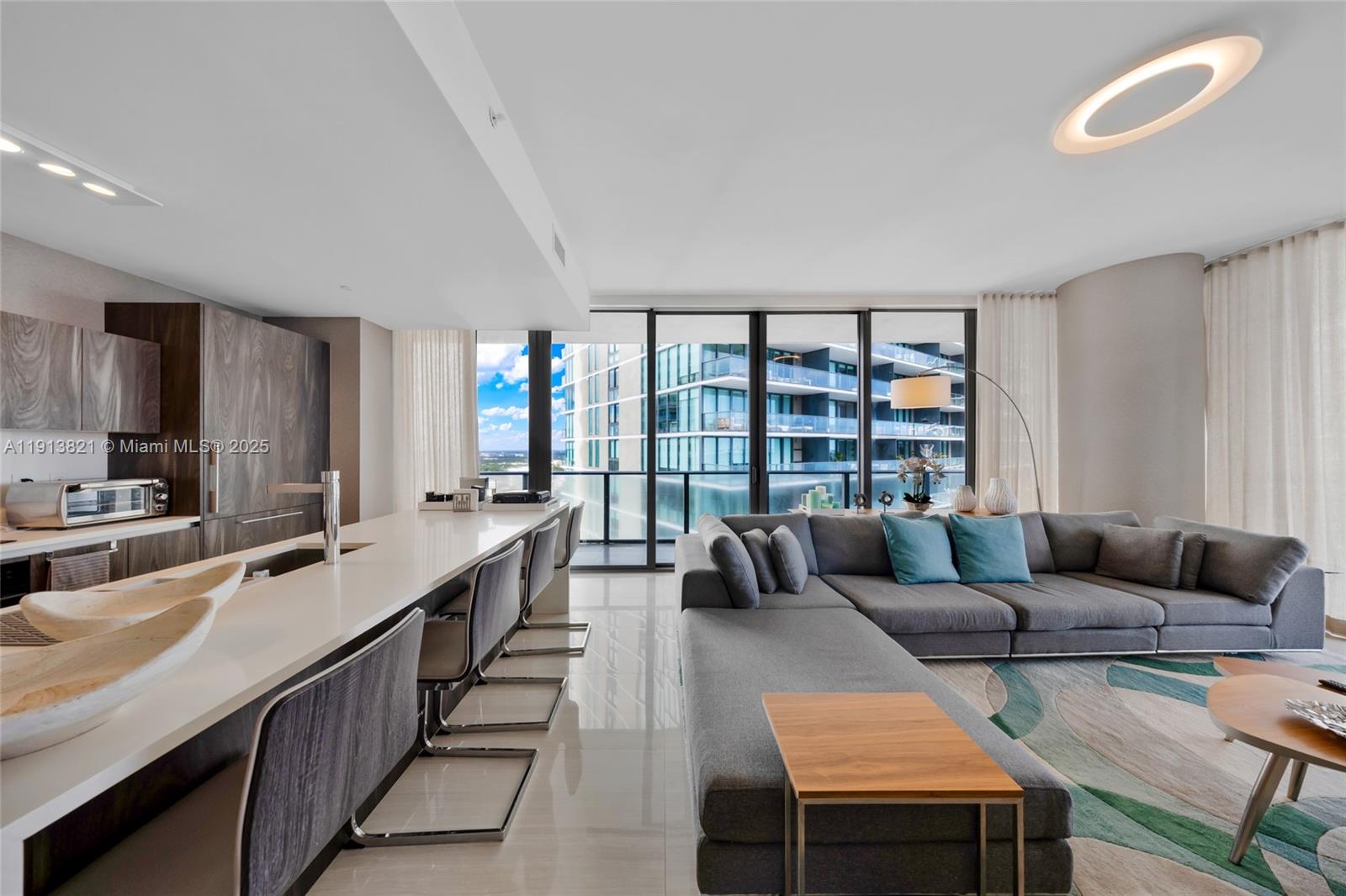 A modern open-concept living room and kitchen featuring a gray sectional sofa and breakfast bar — 480 NE 31st St # 2807, Miami FL 33137, MIAMI, FL