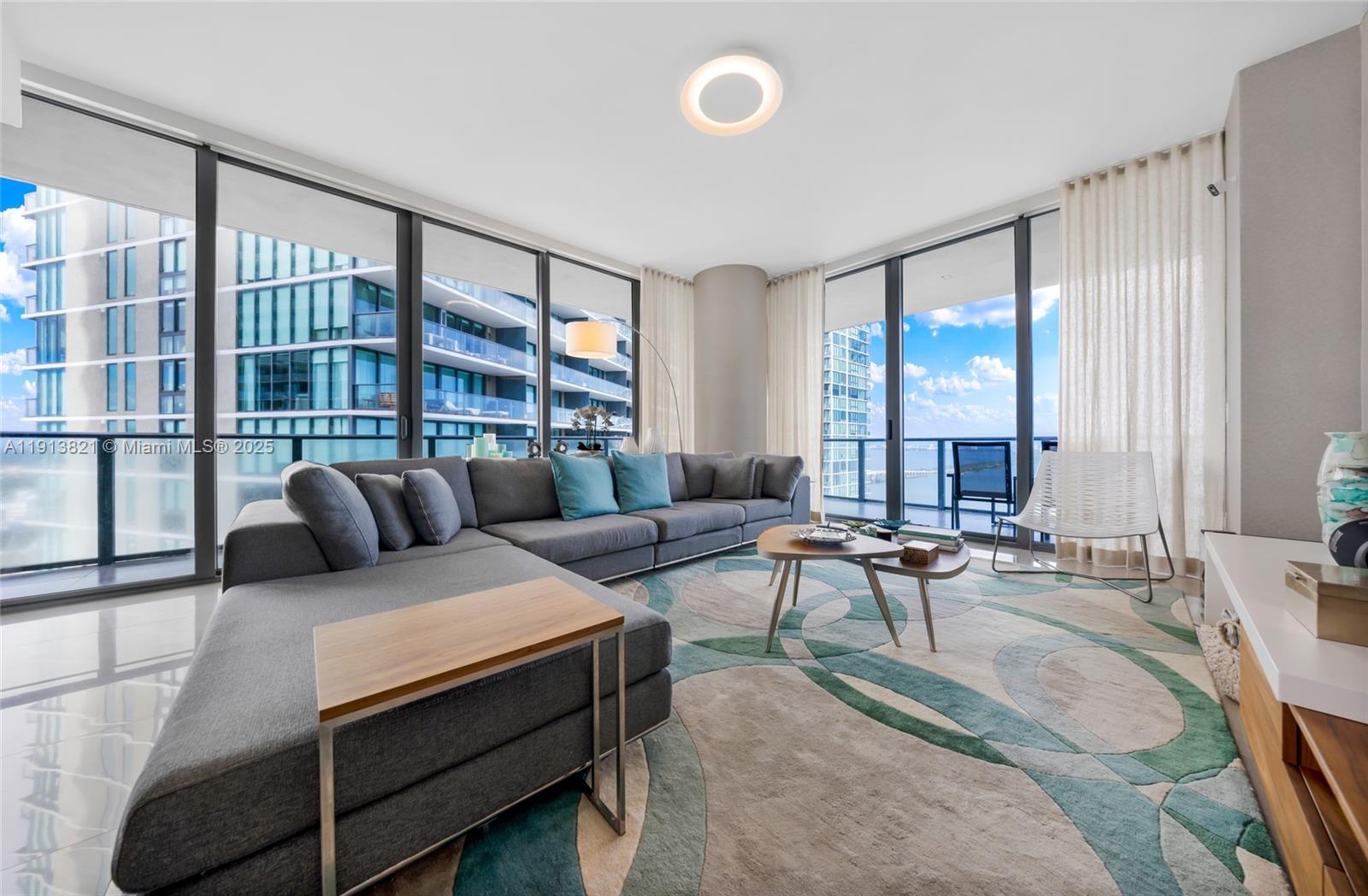 A modern living room features a large gray sectional sofa, patterned rug, and floor-to-ceiling windows — 480 NE 31st St # 2807, Miami FL 33137, MIAMI, FL