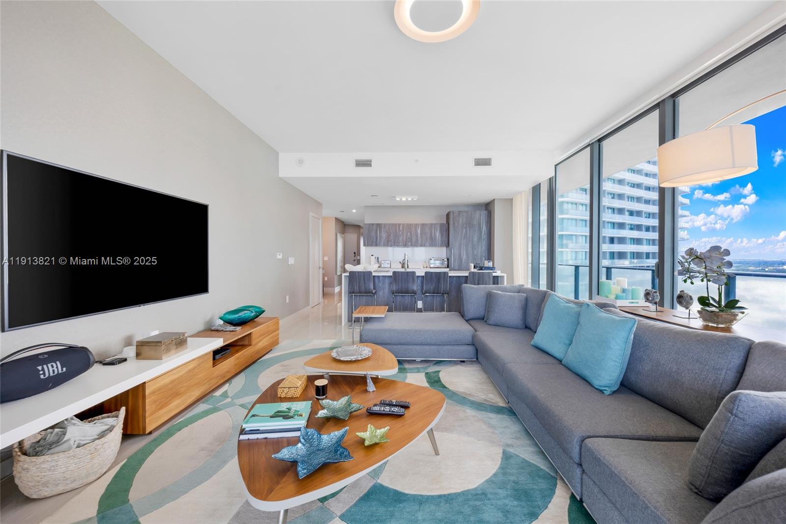 A modern living room features a large sectional sofa, a television, and floor-to-ceiling windows — 480 NE 31st St # 2807, Miami FL 33137, MIAMI, FL