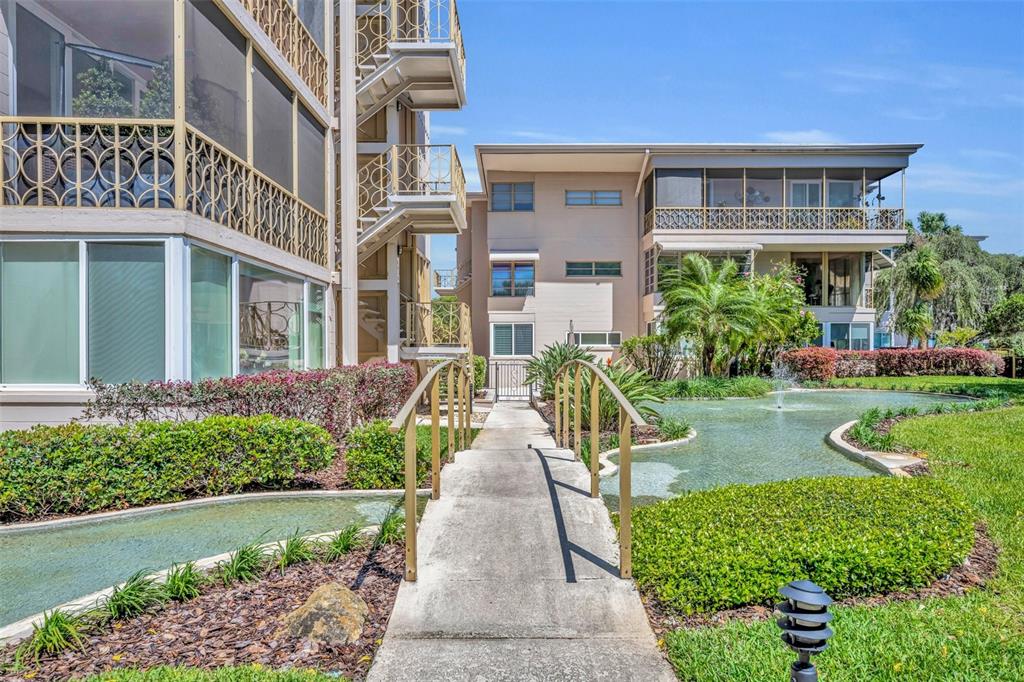 A concrete footbridge crosses a small pond toward a multi-story apartment building with balconies — 311 E MORSE BOULEVARD UNIT 6-12, WINTER PARK, FL