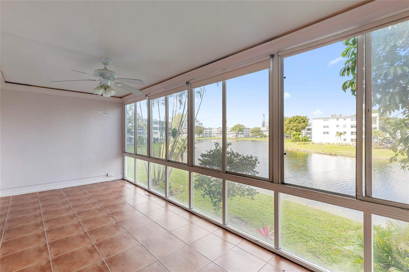 A sunroom with wicker furniture, a television, and large windows overlooking a lake and buildings — 2122 Cambridge F # 2122, Deerfield Beach FL 33442, DEERFIELD BEACH, FL