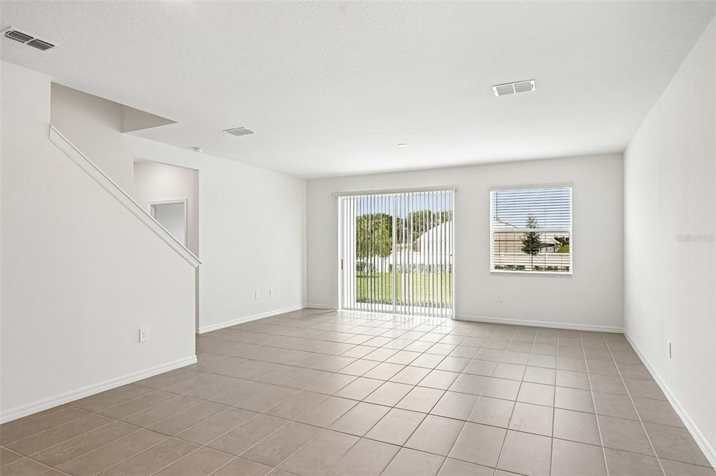 An empty living room features white walls, tile flooring, a staircase, and sliding glass doors — 4606 OUTHAUL RUN, PALMETTO, FL