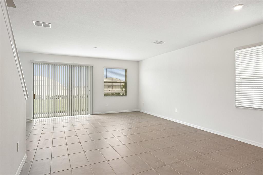 An empty living room features light-colored tile flooring, white walls, and sliding glass doors — 4606 OUTHAUL RUN, PALMETTO, FL