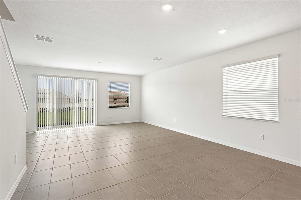 An empty living room features light-colored tile flooring, white walls, and sliding glass doors — 4606 OUTHAUL RUN, PALMETTO, FL
