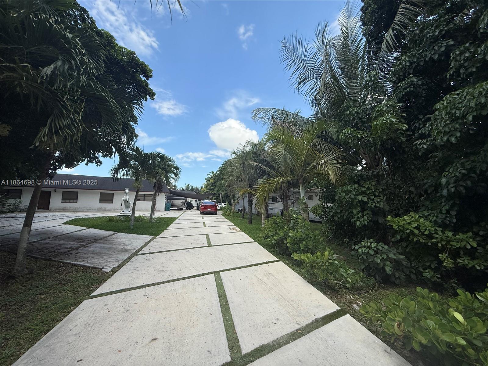 A paved driveway leads toward a house and parked vehicles surrounded by lush tropical landscaping — 15765 SW 206th Ave, Miami FL 33187, MIAMI, FL