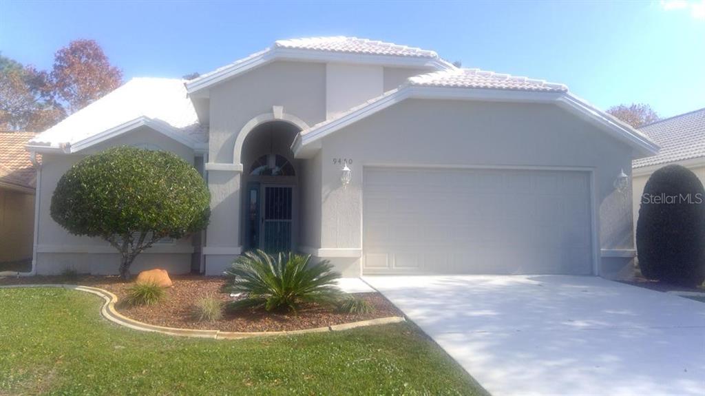 A single-story house with a white tiled roof, light-colored stucco exterior, and a two-car garage — 9450 MISSISSIPPI RUN, WEEKI WACHEE, FL