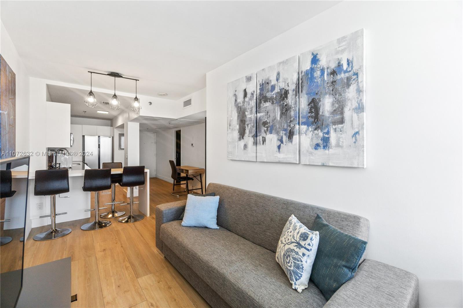 A modern living room features a gray sofa, abstract wall art, and a kitchen island — 100 Lincoln Rd # 1627, Miami Beach FL 33139, MIAMI BEACH, FL