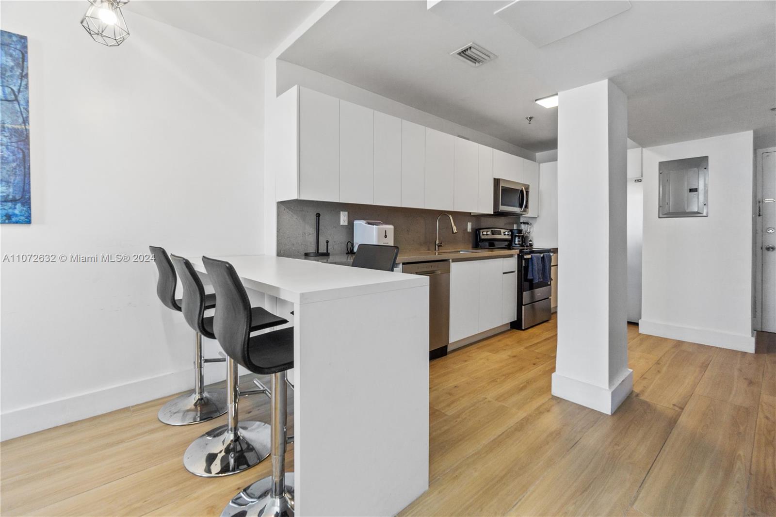 A modern kitchen features white cabinets, stainless steel appliances, and a breakfast bar with stools — 100 Lincoln Rd # 1627, Miami Beach FL 33139, MIAMI BEACH, FL