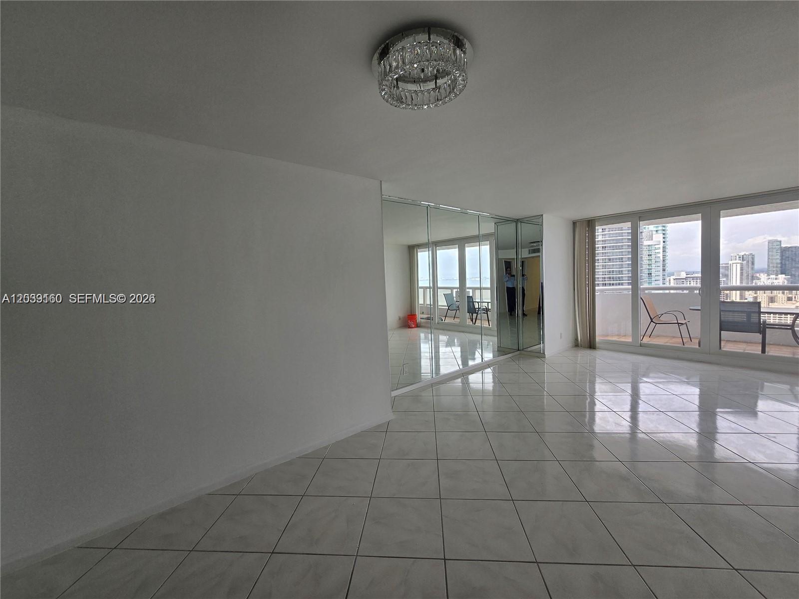 A bright living area features white tile floors, a crystal chandelier, and mirrored wall panels — MIAMI, FL