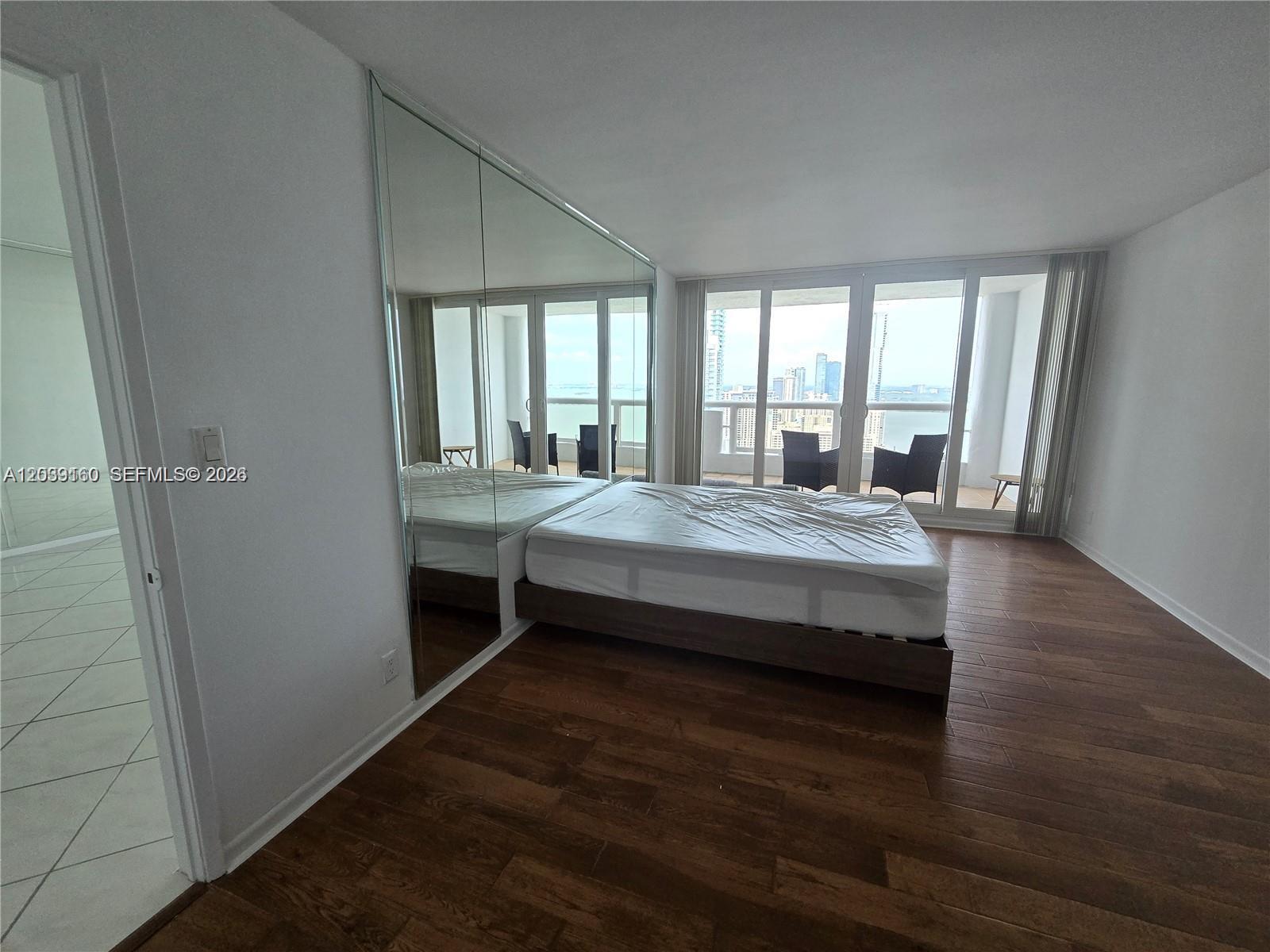 A bedroom features a platform bed, mirrored closet doors, and a balcony with city views — MIAMI, FL