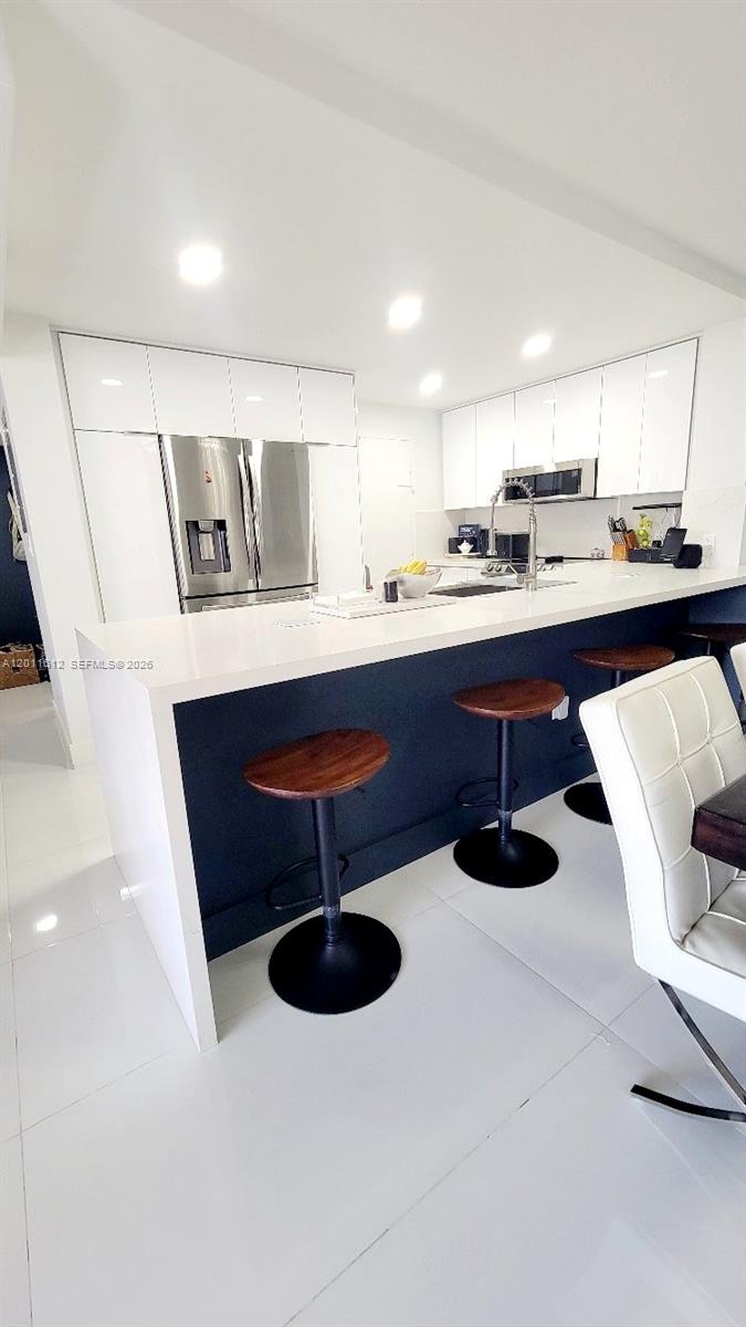 A modern kitchen features white cabinetry, a large island with bar stools, and stainless appliances — 250 Galen Dr # 43, Key Biscayne FL 33149, KEY BISCAYNE, FL