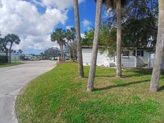 A white mobile home sits on a grassy lot with palm trees under a blue sky — 61 MOURNINGDOVE COURT, ELLENTON, FL