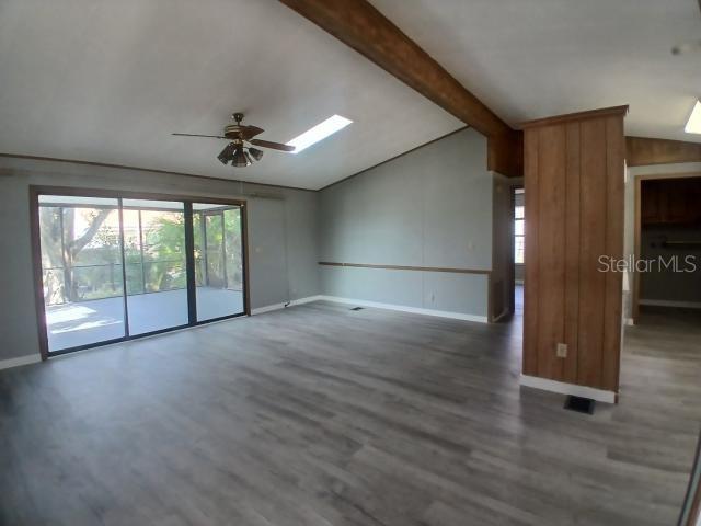A living room features gray wood-look flooring, a vaulted ceiling with beams, and sliding glass doors — 61 MOURNINGDOVE COURT, ELLENTON, FL
