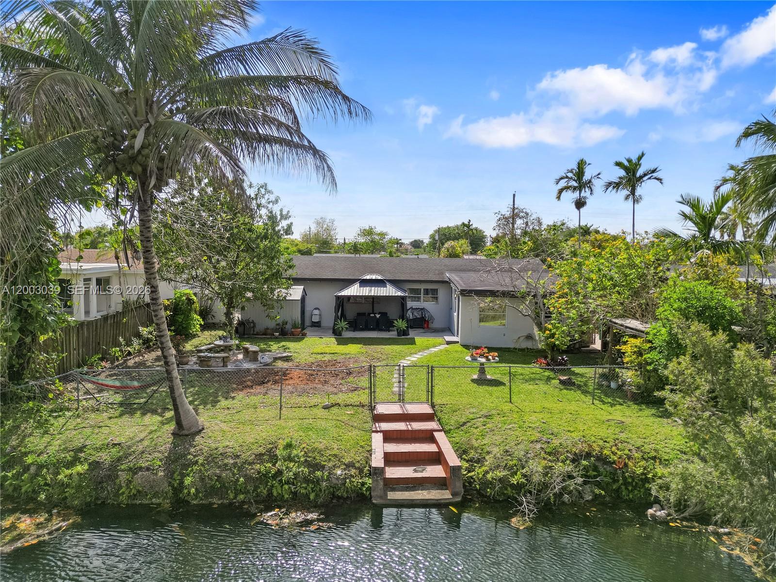 A backyard with a canal, stairs, a gazebo, and a palm tree behind a house — 3921 SW 124th Ct, Miami FL 33175, MIAMI, FL