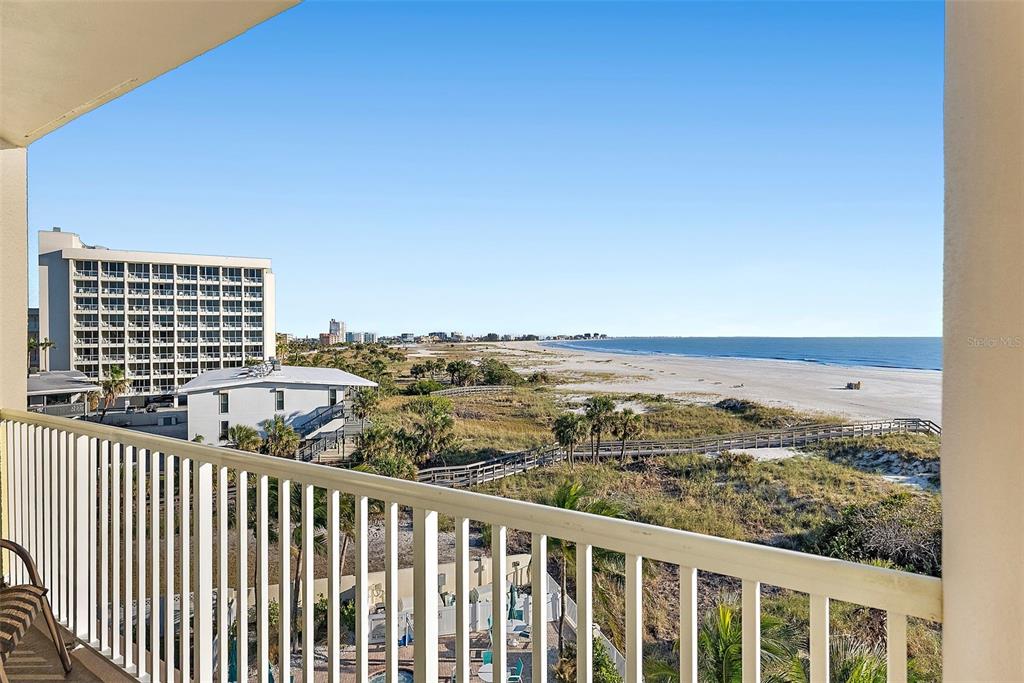 A balcony view overlooks a sandy beach, dunes, and coastal buildings under a clear sky — 12000 GULF BOULEVARD UNIT 501-W, TREASURE ISLAND, FL