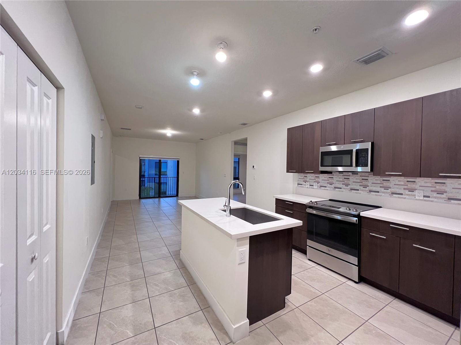 A kitchen features dark wood cabinets, stainless steel appliances, a white island, and tile flooring — 8265 NW 41st St # 405, Doral FL 33166, DORAL, FL