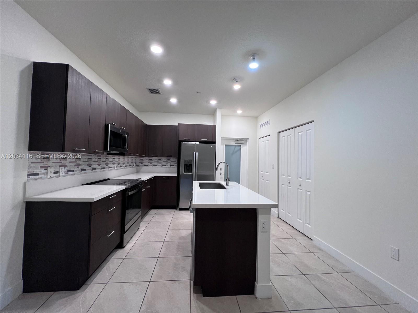 A modern kitchen features dark wood cabinets, white countertops, stainless steel appliances, and tile flooring — 8265 NW 41st St # 405, Doral FL 33166, DORAL, FL