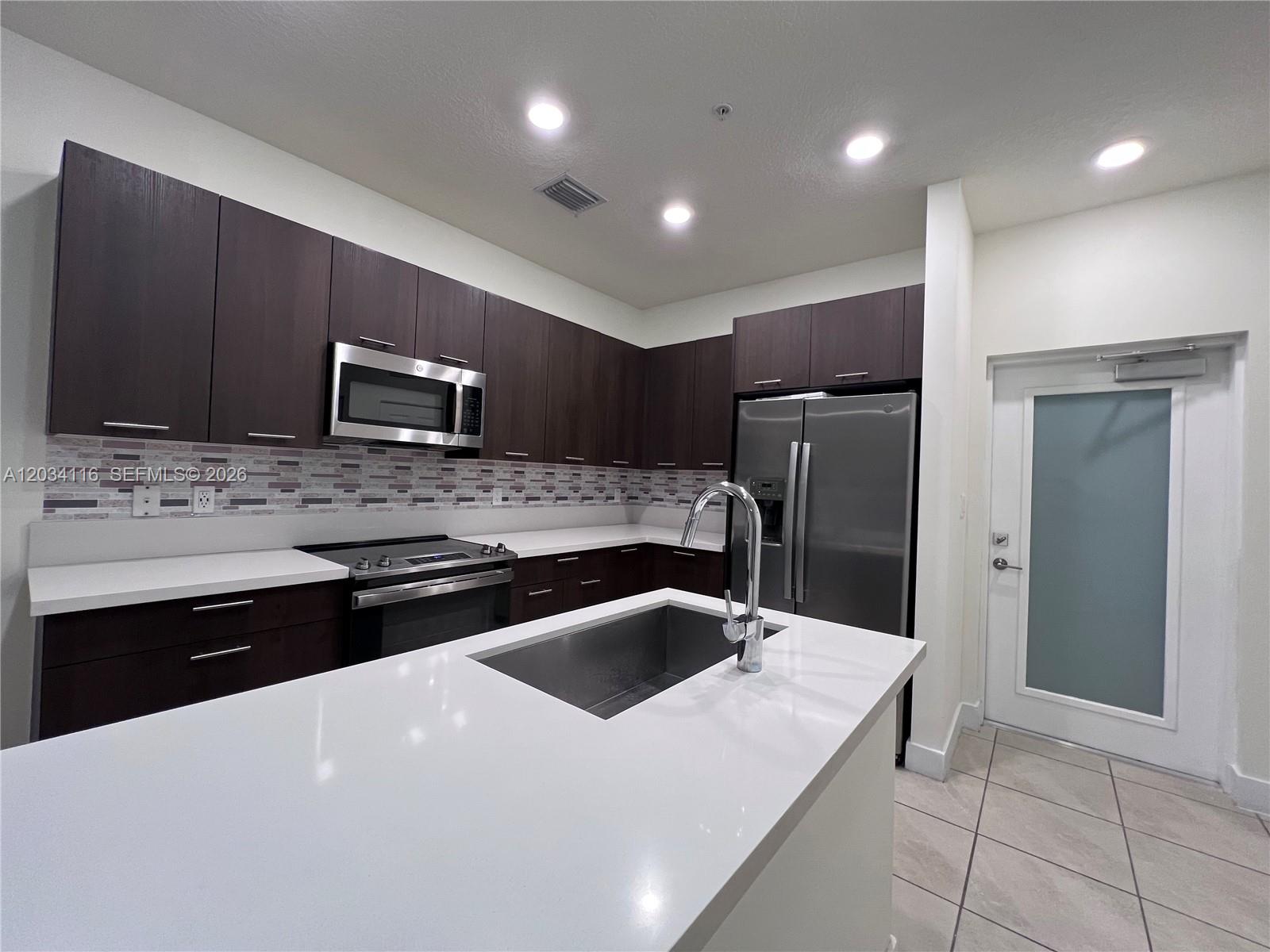A modern kitchen features dark wood cabinetry, white countertops, stainless steel appliances, and a central island — 8265 NW 41st St # 405, Doral FL 33166, DORAL, FL