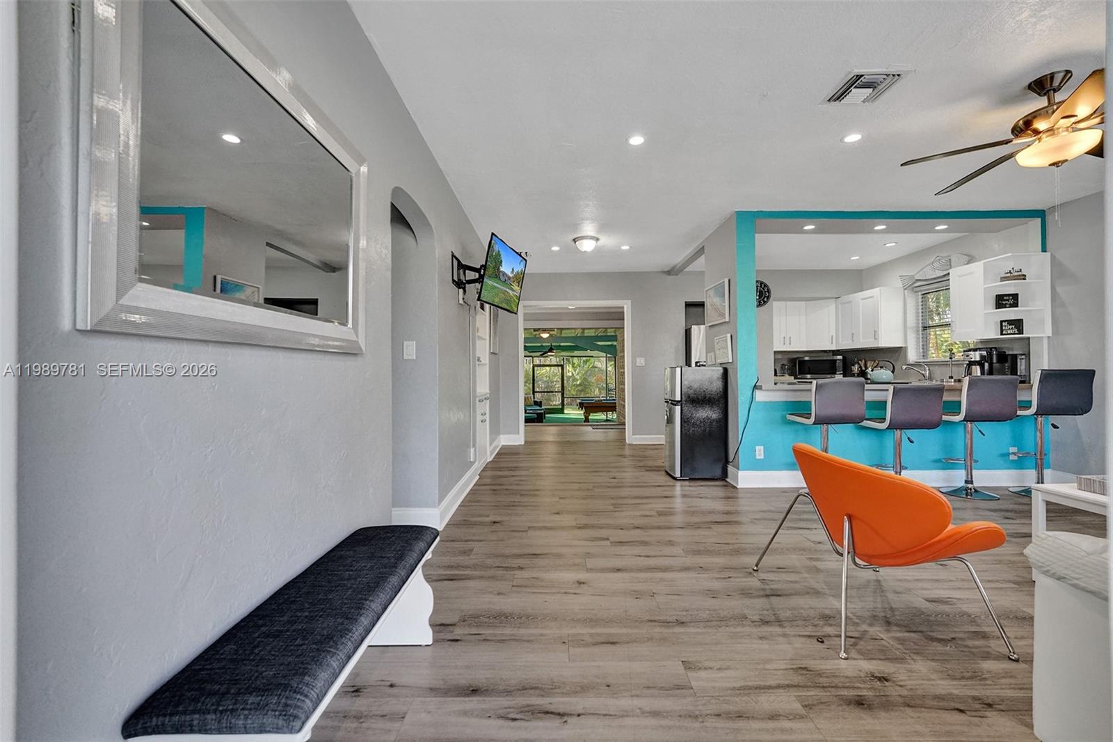 A living area with gray walls, wood-look flooring, and a kitchen with a turquoise accent wall — 529 NW 8th St, Dania Beach FL 33004, DANIA BEACH, FL