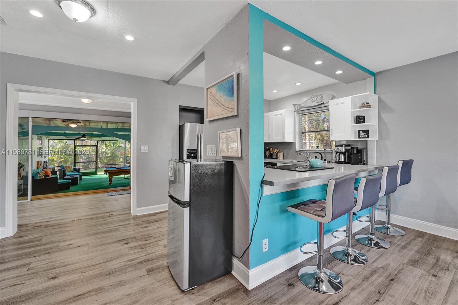 A kitchen with a breakfast bar and teal accent wall opens to a sunroom — 529 NW 8th St, Dania Beach FL 33004, DANIA BEACH, FL
