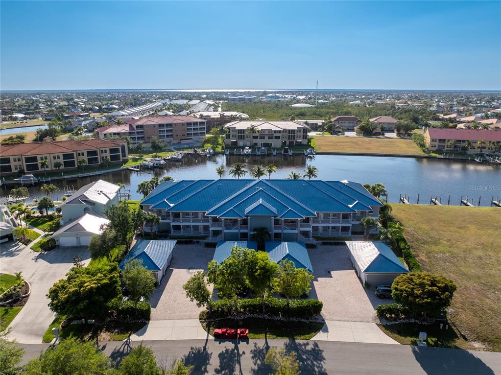 An aerial view shows a multi-story residential building with a blue roof near water — 3311 WOOD THRUSH DRIVE UNIT 113, PUNTA GORDA, FL