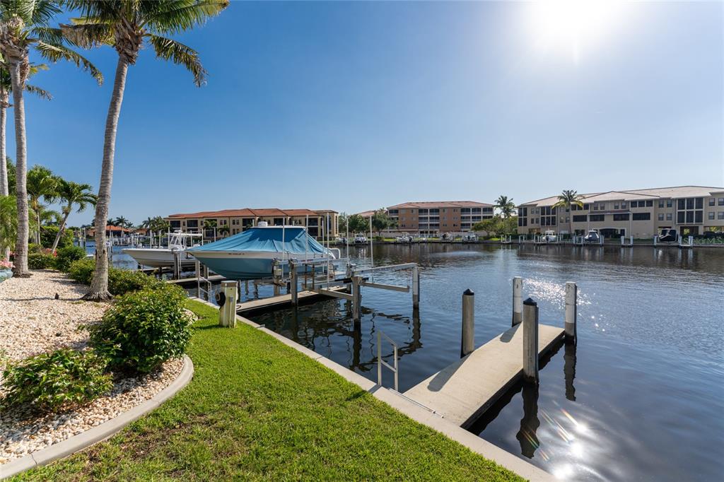 A canal view featuring a boat lift, a private dock, and multi-story residential buildings — 3311 WOOD THRUSH DRIVE UNIT 113, PUNTA GORDA, FL