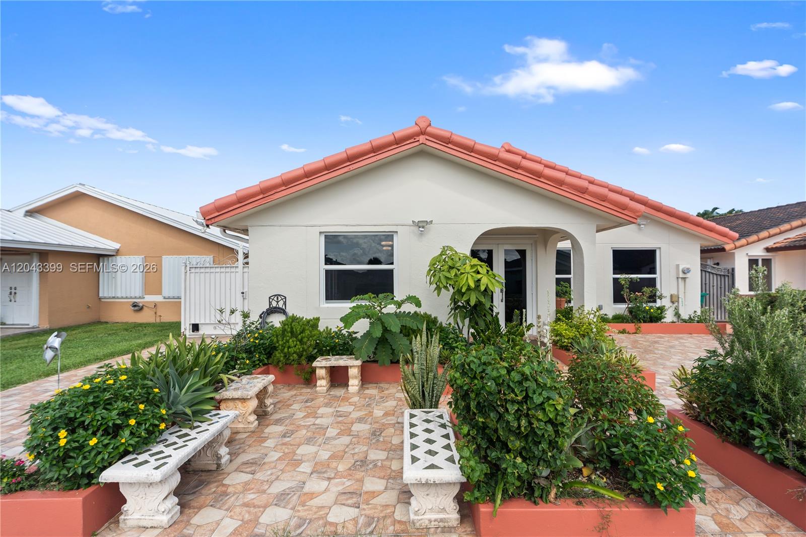 A single-story house with a tiled roof, a paved patio, and various garden plants — 910 SW 140th Ave, Miami FL 33184, MIAMI, FL