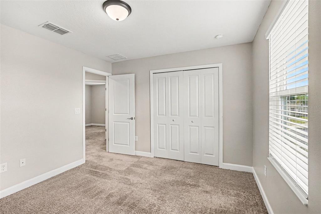 A bedroom with beige carpet, light gray walls, a closet, and a doorway to another room — 490 BRUNSWICK DRIVE, DAVENPORT, FL